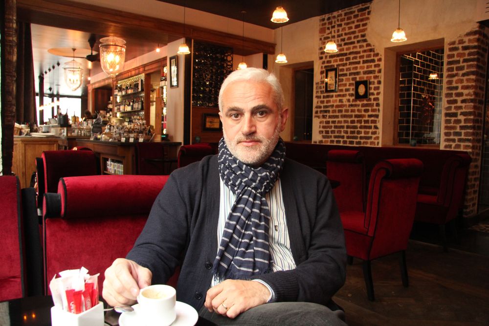 Man with white hair and beard sips coffee in a cozy cafe.